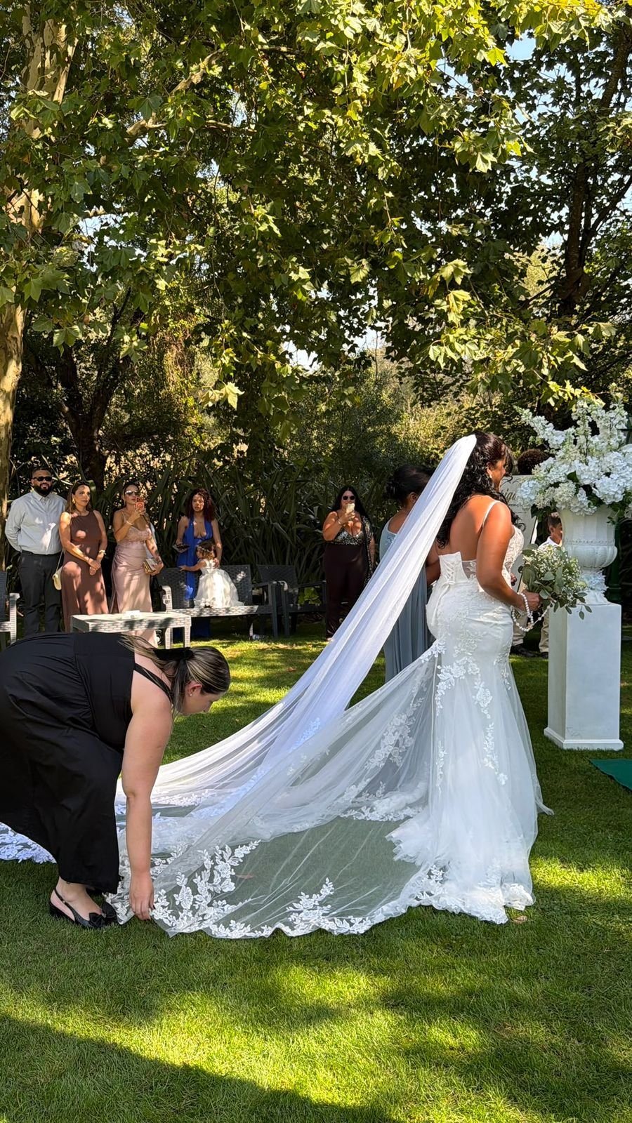 Wedding planner a compor a cauda do véu da noiva durante a entrada para a cerimónia ao ar livre